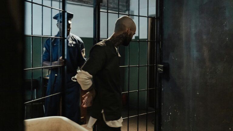 Police officer escorting a handcuffed prisoner through a dimly lit jail corridor.