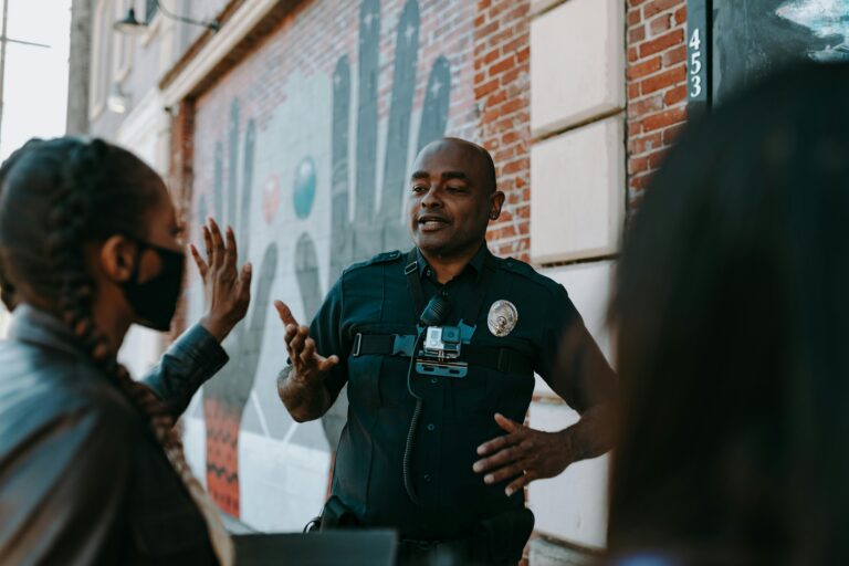 Police officer conversing with people on the street near a brick wall mural.