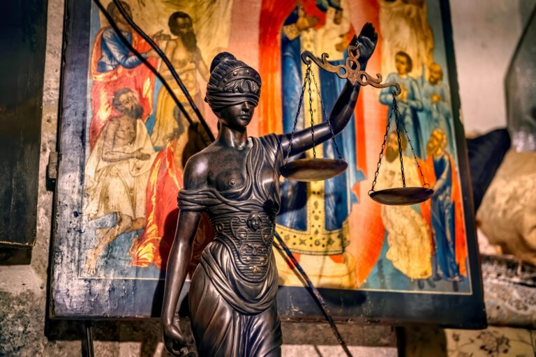 A blindfolded statue representing justice holding scales, set against an ornate background in Jerusalem.
