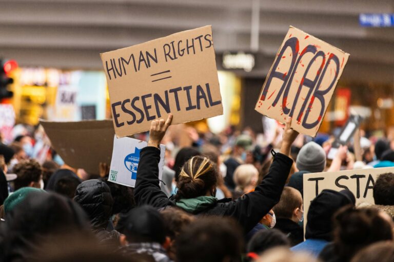A crowd gathers in Melbourne for a protest advocating human rights, holding signs with powerful messages.