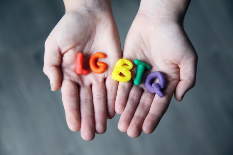 Close-up of hands holding colorful letters representing LGBTQ pride.