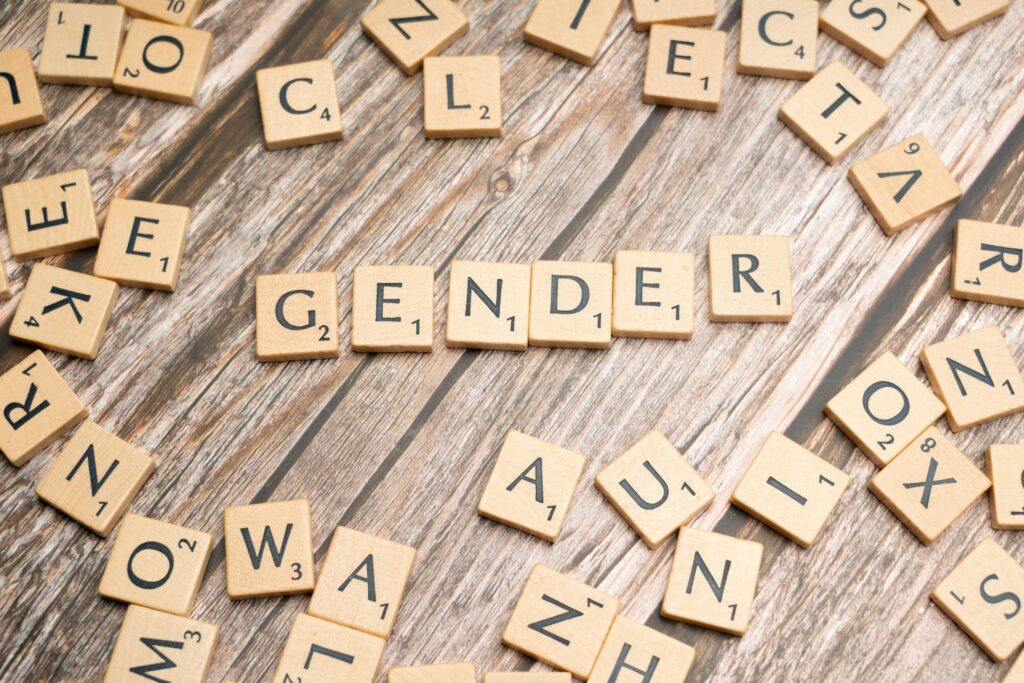 Wooden letter tiles spelling 'gender' on a wooden background, depicting identity and expression.