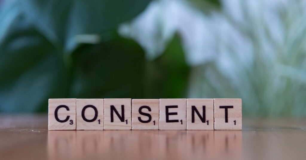 Close-up of Scrabble tiles spelling 'Consent' on a wooden table with a green blurred background.