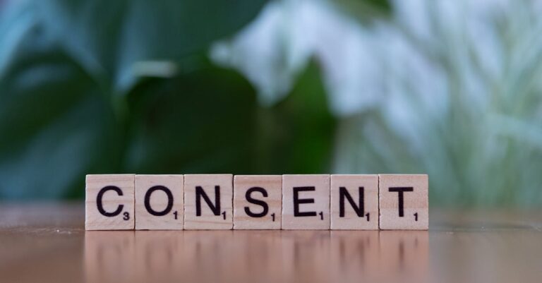 Close-up of Scrabble tiles spelling 'Consent' on a wooden table with a green blurred background.