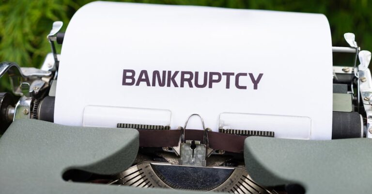 Close-up of a typewriter with the word 'BANKRUPTCY' on paper, surrounded by greenery.