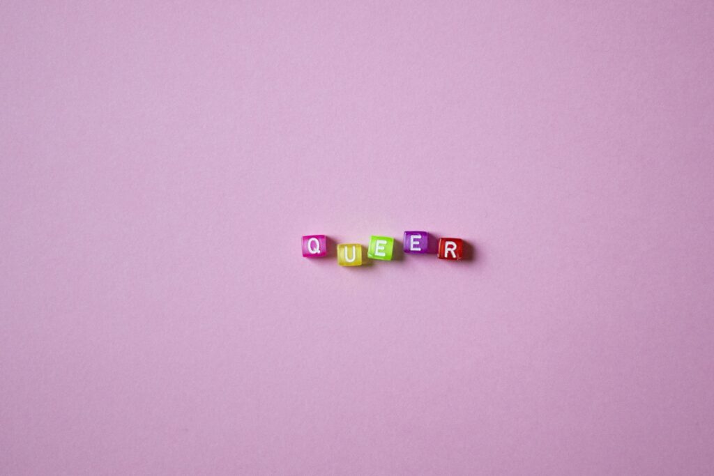 A vibrant display of beads spelling 'QUEER' on a pink background, symbolizing LGBTQ pride and diversity.