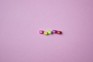 A vibrant display of beads spelling 'QUEER' on a pink background, symbolizing LGBTQ pride and diversity.