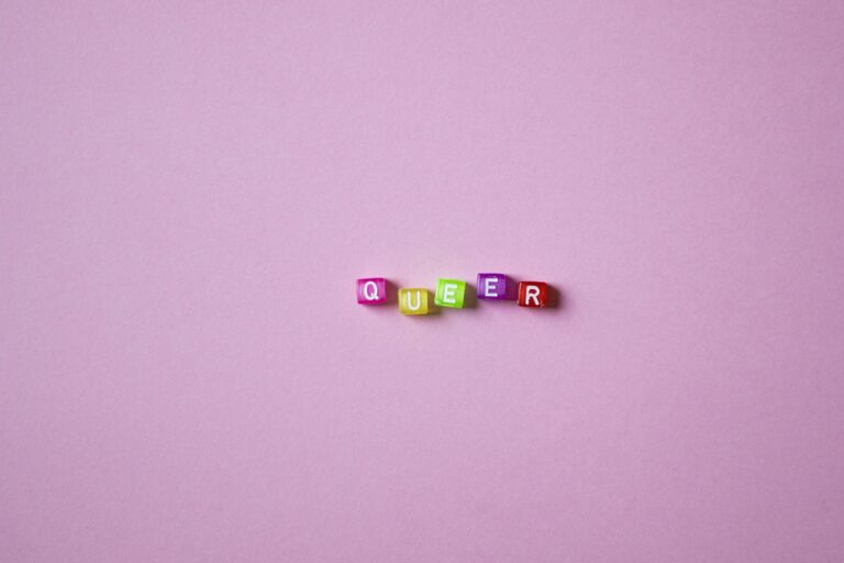 A vibrant display of beads spelling 'QUEER' on a pink background, symbolizing LGBTQ pride and diversity.