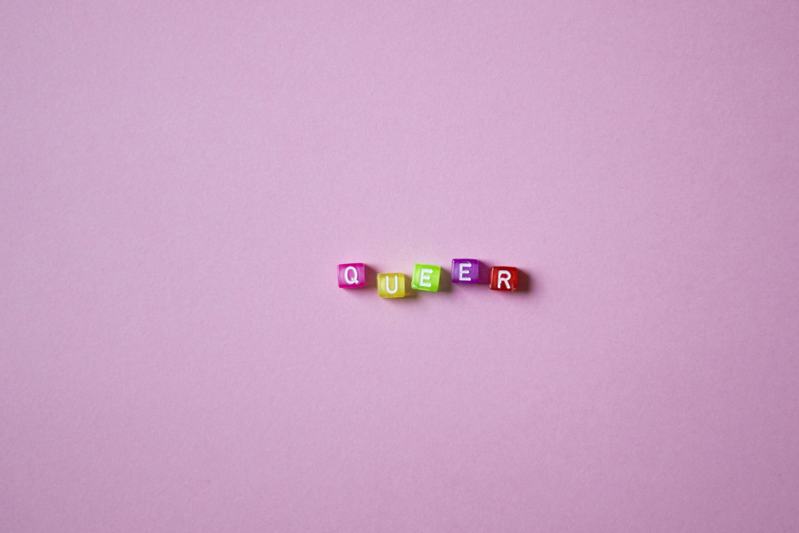 A vibrant display of beads spelling 'QUEER' on a pink background, symbolizing LGBTQ pride and diversity.