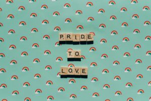 Scrabble tiles spelling 'Pride to Love' on a rainbow background, celebrating LGBT pride.