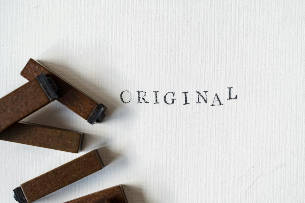 Wooden stamps spelling 'ORIGINAL' on textured paper, minimalistic design.