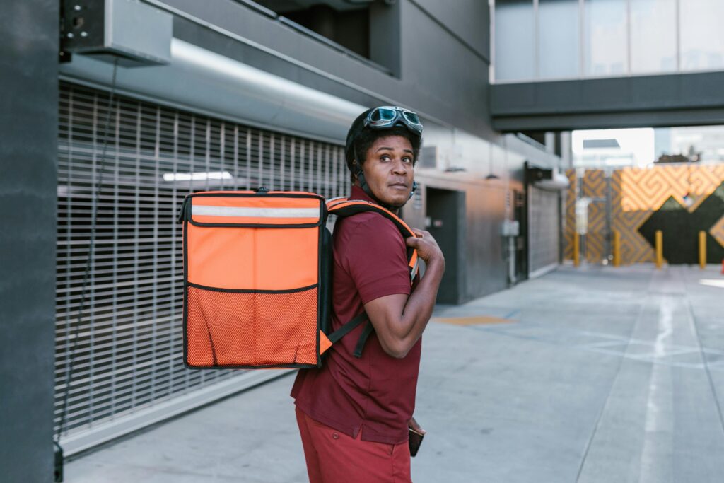 Courier with helmet and delivery bag in an urban alley, looking back.