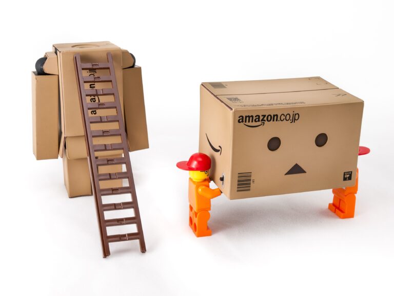 Unique cardboard box figures interacting with a ladder on a white background, showcasing creativity and playfulness.