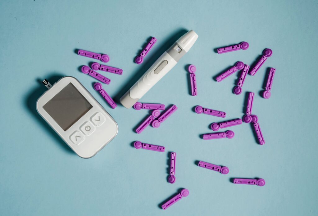 Top view of lancets scattered around blood glucose meter and lancing device on blue background